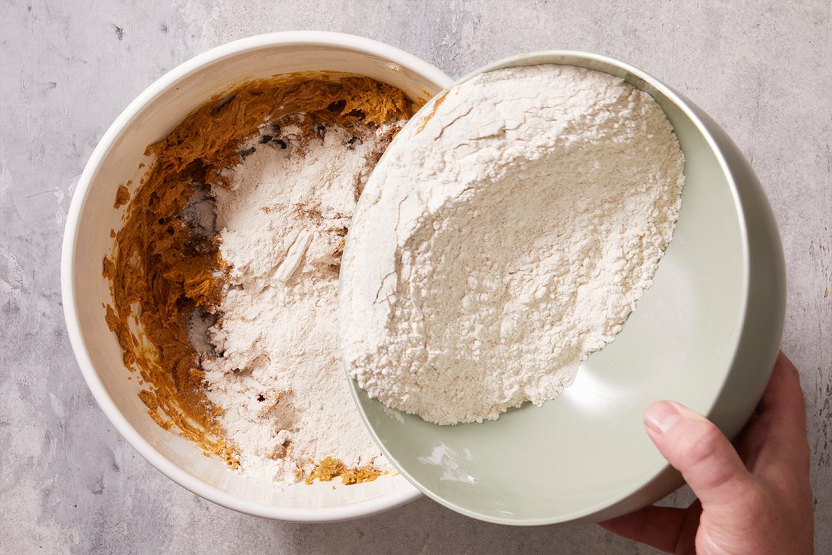 Overhead shot of flour being poured into the wet cookie mixture for combining.