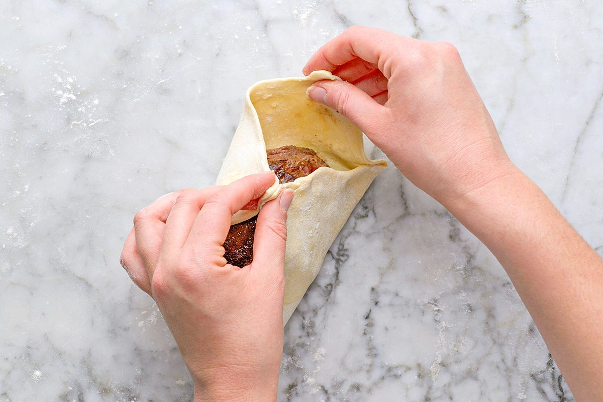 Overhead shot of hands folding dough around a filling on a marble countertop, preparing to seal it;