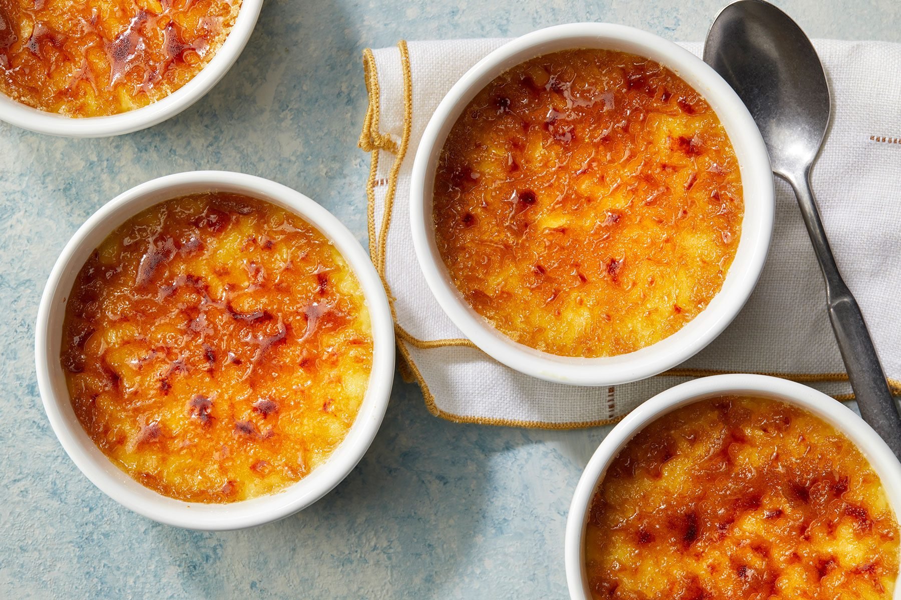 overhead shot of Creme Brulee in small bowls with a spoon kept on side.