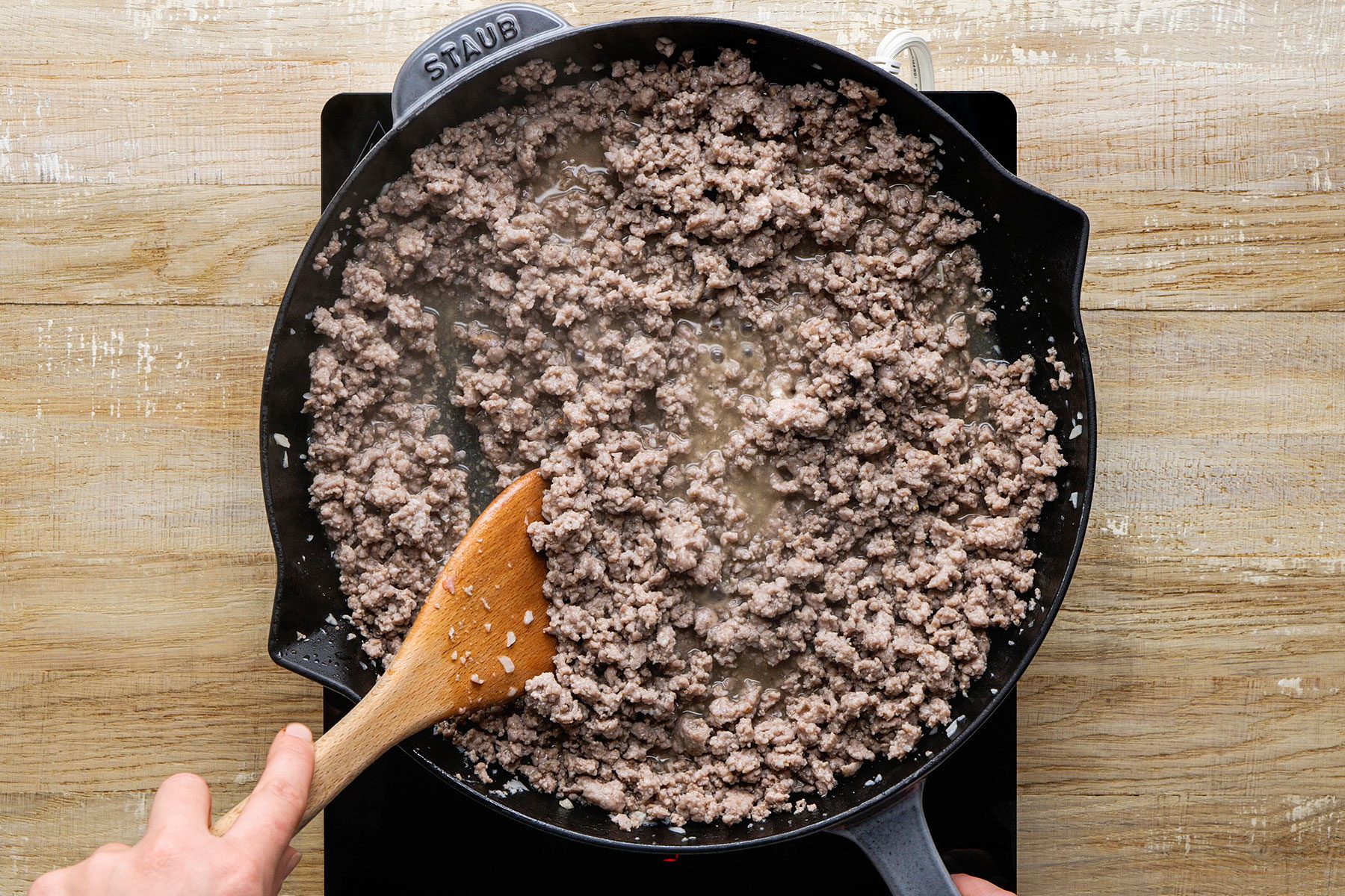 Adding broth mixture to the pork with spices in a large skillet.