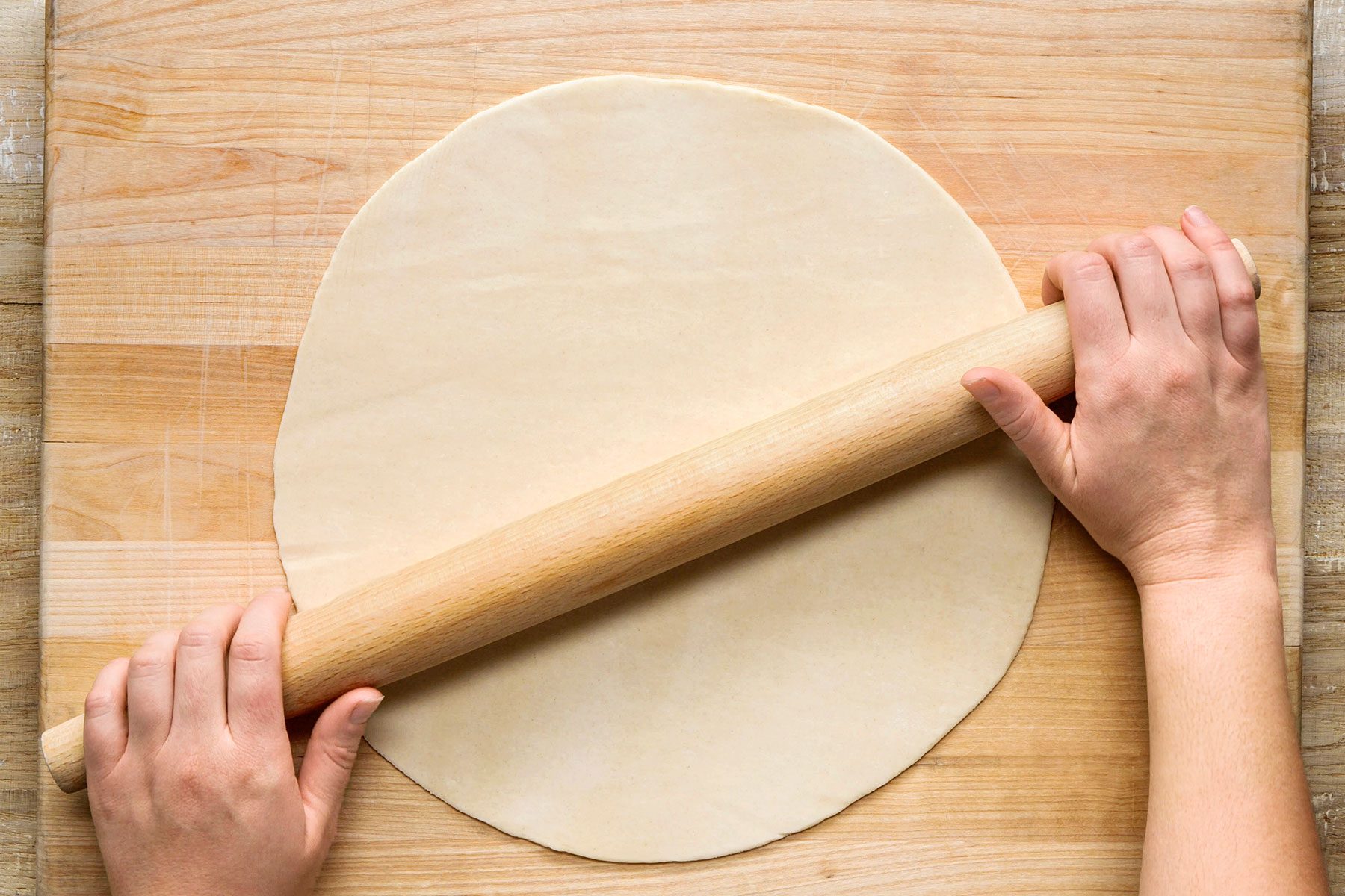 On a lightly floured work surface, rolling a pie dough out into a 12-inch circle using a rolling pin.