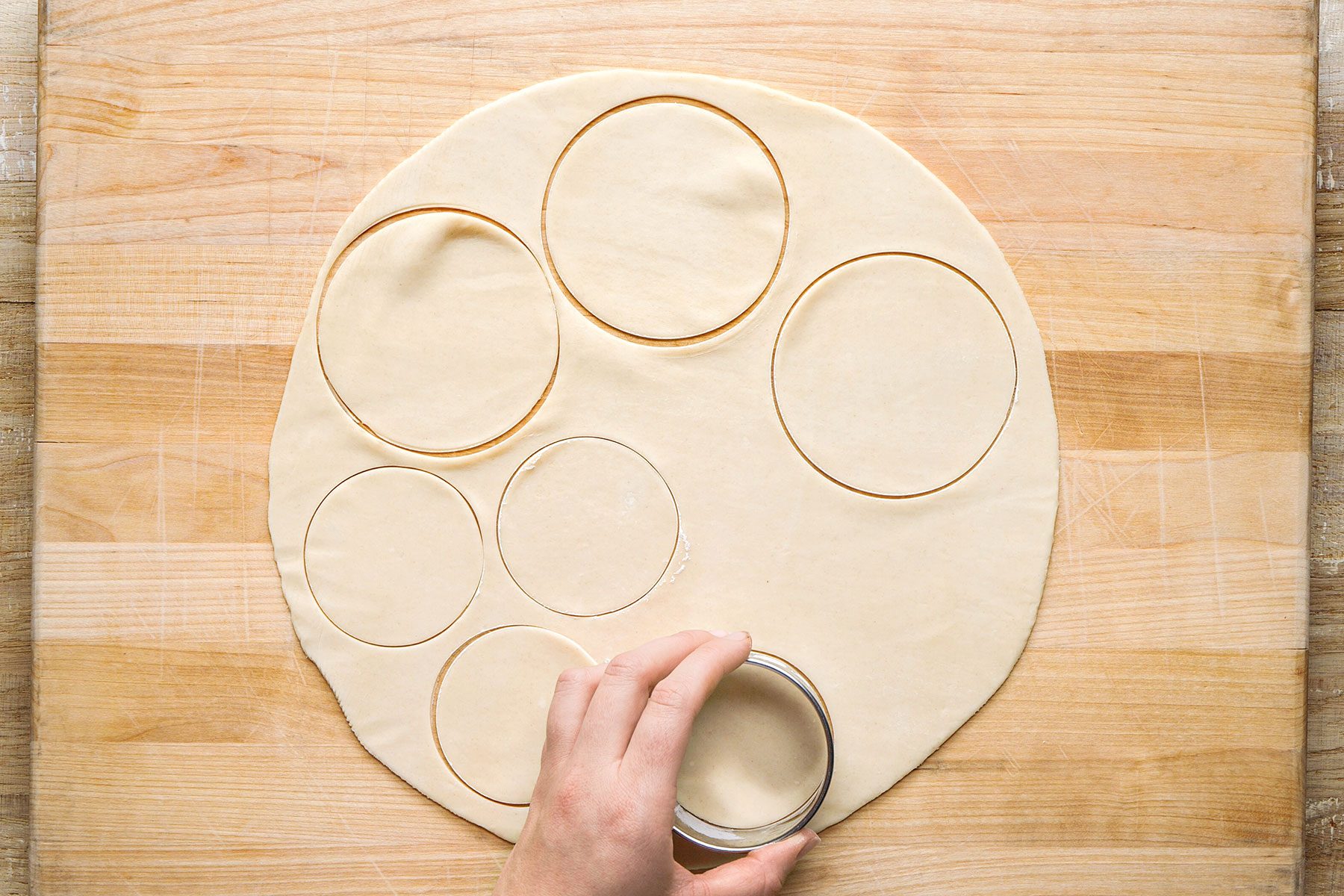 Using floured round cookie cutters, cutthing twenty 4-inch circles and twenty 2-3/4-inch circles on a wooden board.