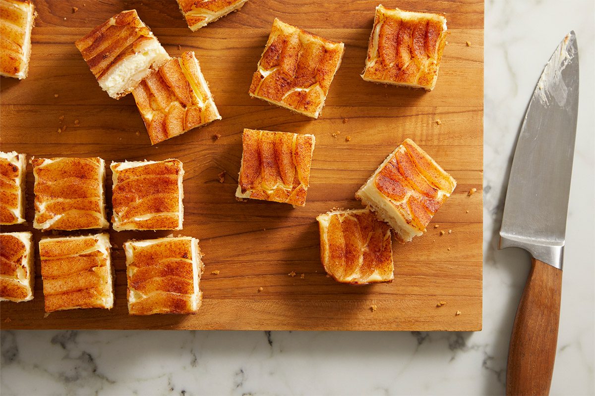 Overhead shot of perfectly cut Pear Custard Bars arranged in a grid pattern on a wooden board next to a knife.