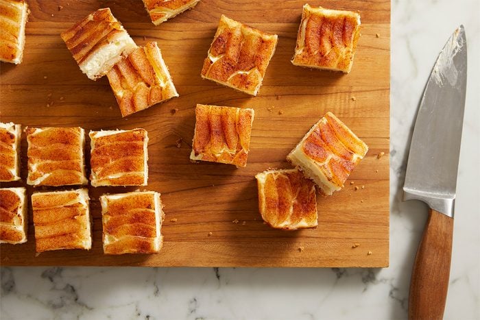 Overhead shot of perfectly cut Pear Custard Bars arranged in a grid pattern on a wooden board next to a knife.
