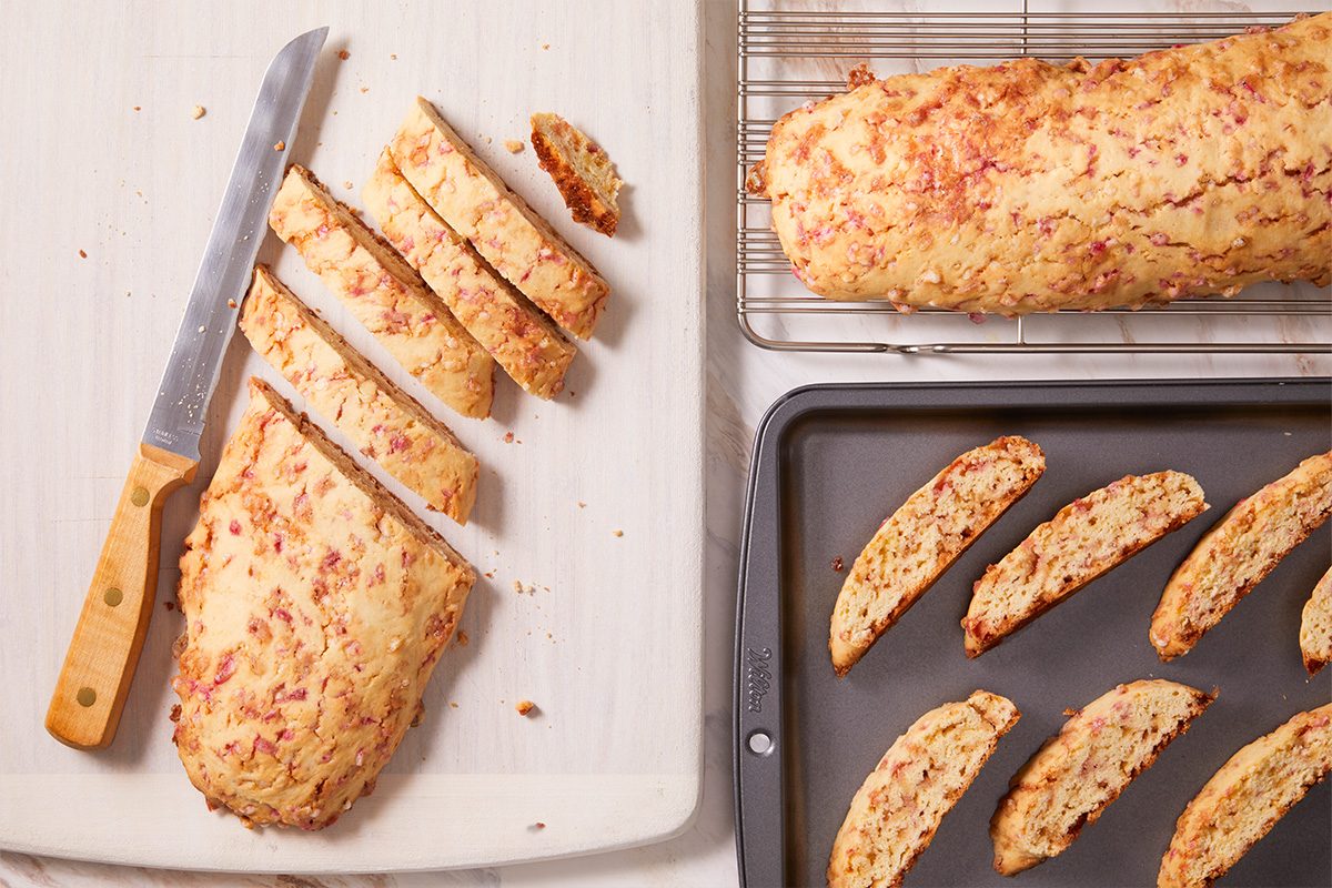 Overhead shot of baked biscotti logs sliced into even pieces with a serrated knife on a baking tray.