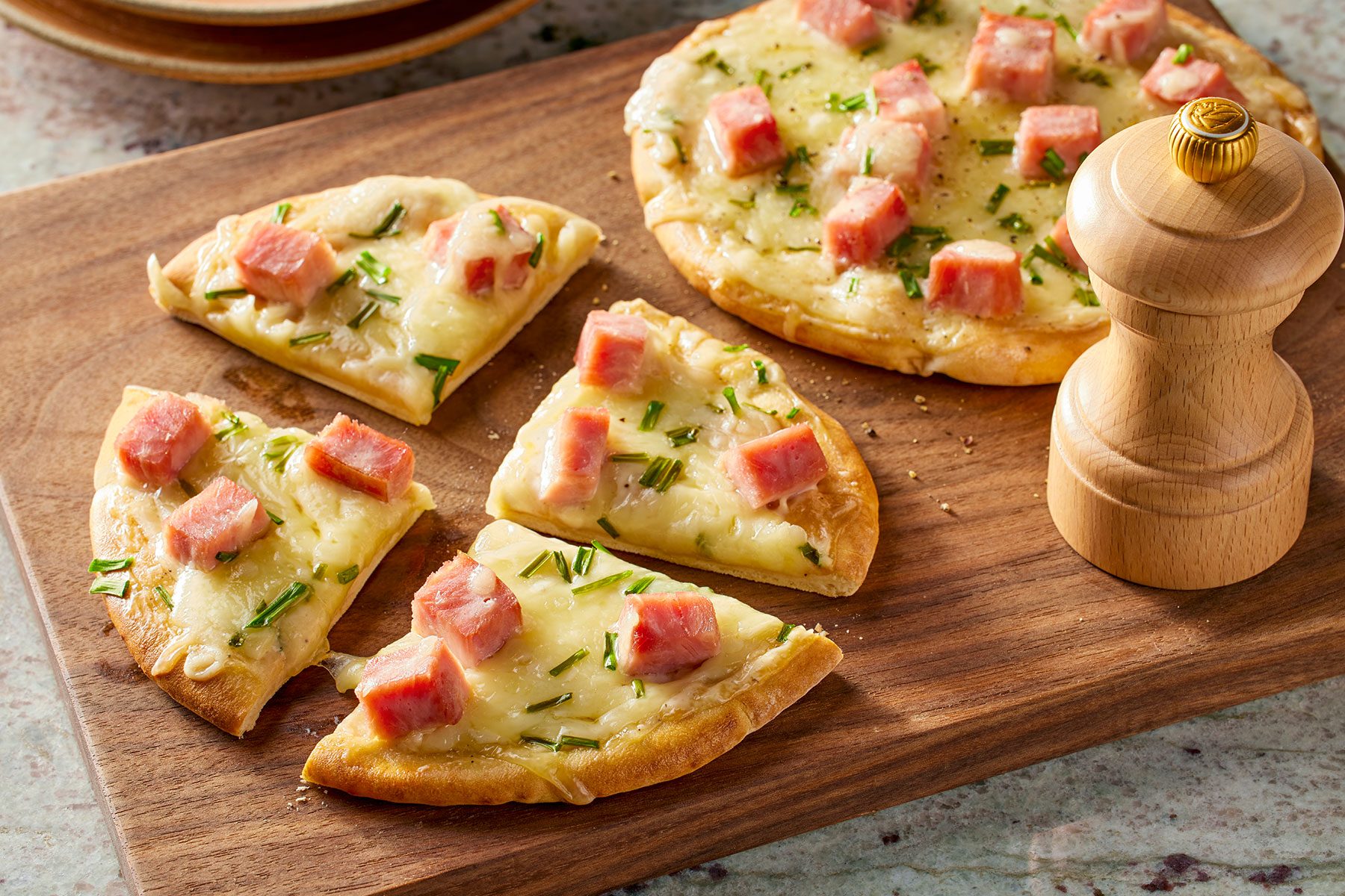 Baked Pita Bread Pizza cut into pieces on a wooden board with a pepper crusher on side.