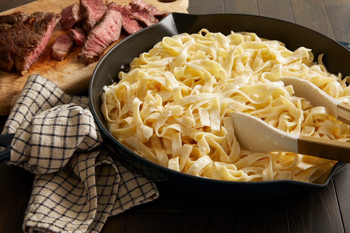 Overhead shot of creamy Alfredo pasta plated in a bowl, ready for topping, with a fork resting beside it.