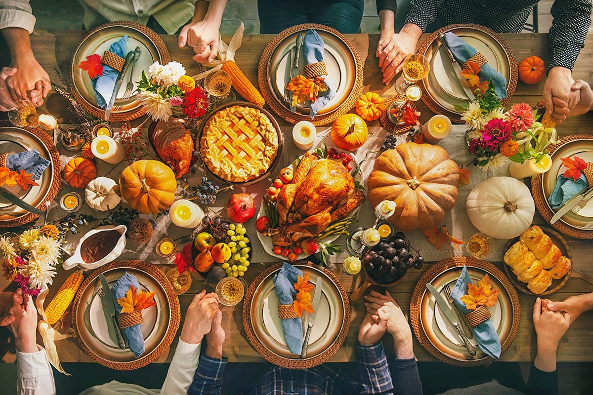 Group of friends or family members giving thanks to God at festive turkey dinner table together.