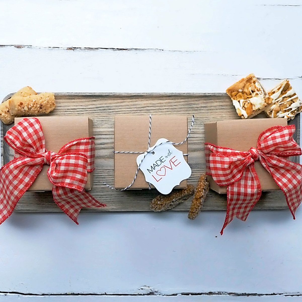 Three brown gift boxes on a wooden tray, two tied with red checkered bows and one with twine and a tag reading