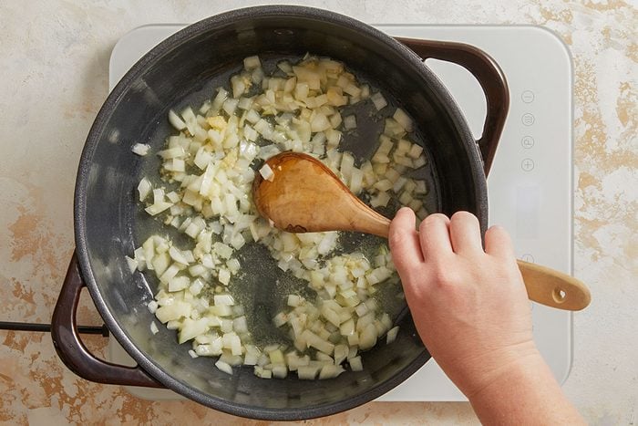 Overhead shot of onions being sautéed in a black pot with a wooden spoon stirring the mixture.