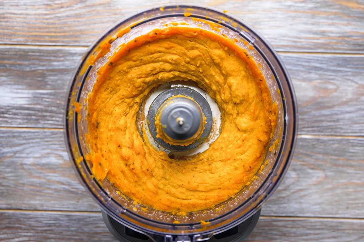 Overhead shot of a food processor blending orange-colored puree on a wooden surface the scene captures the mixing in progress