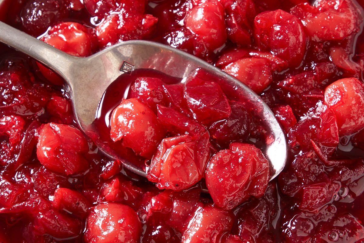 A close-up of a metal spoon scooping thick, chunky red cranberry sauce with whole berries.