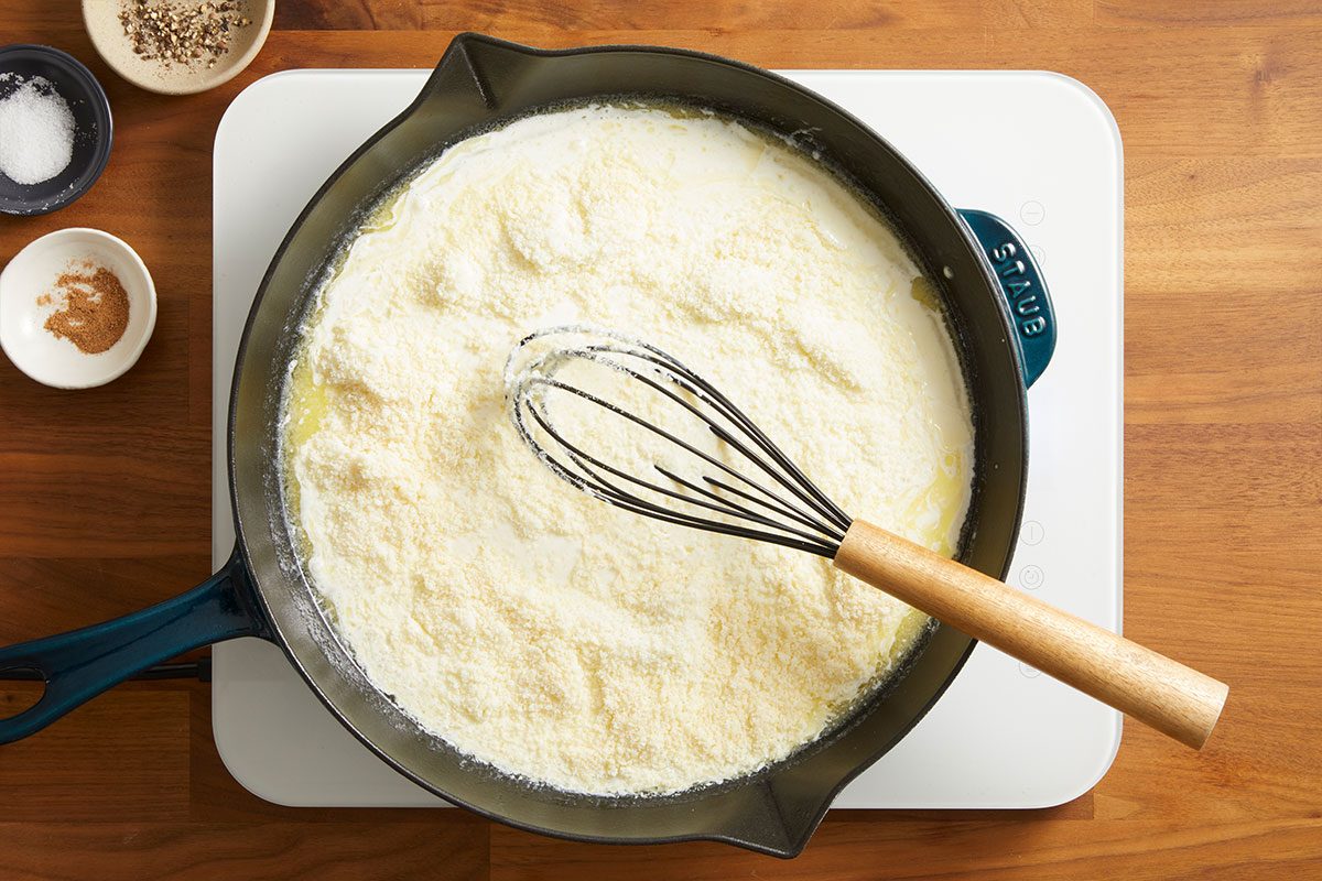 Overhead shot of Alfredo sauce being whisked in a skillet, smooth and creamy in texture.