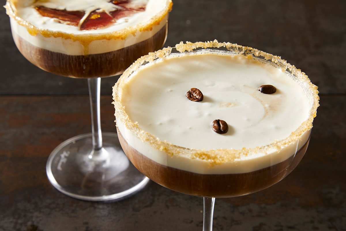 3/4 angle shot of a crème brûlée espresso martini with a caramelized sugar rim and creamy top, garnished with coffee beans, set on a dark surface;