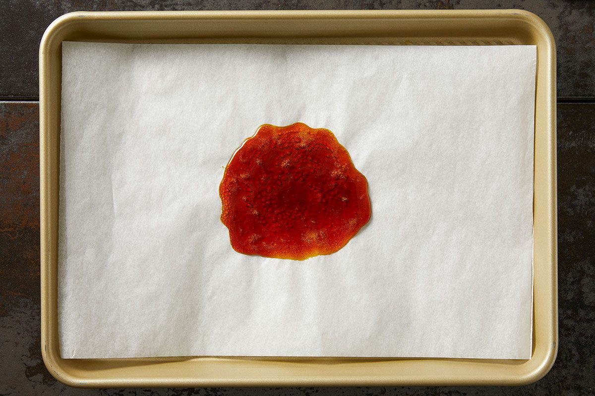 Overhead shot of a spoonful of hot caramel poured onto parchment paper on a baking sheet, cooling and spreading;
