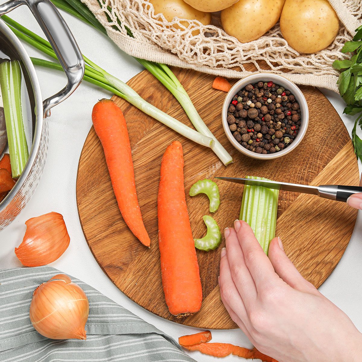 Woman cutting celery at white table, top view