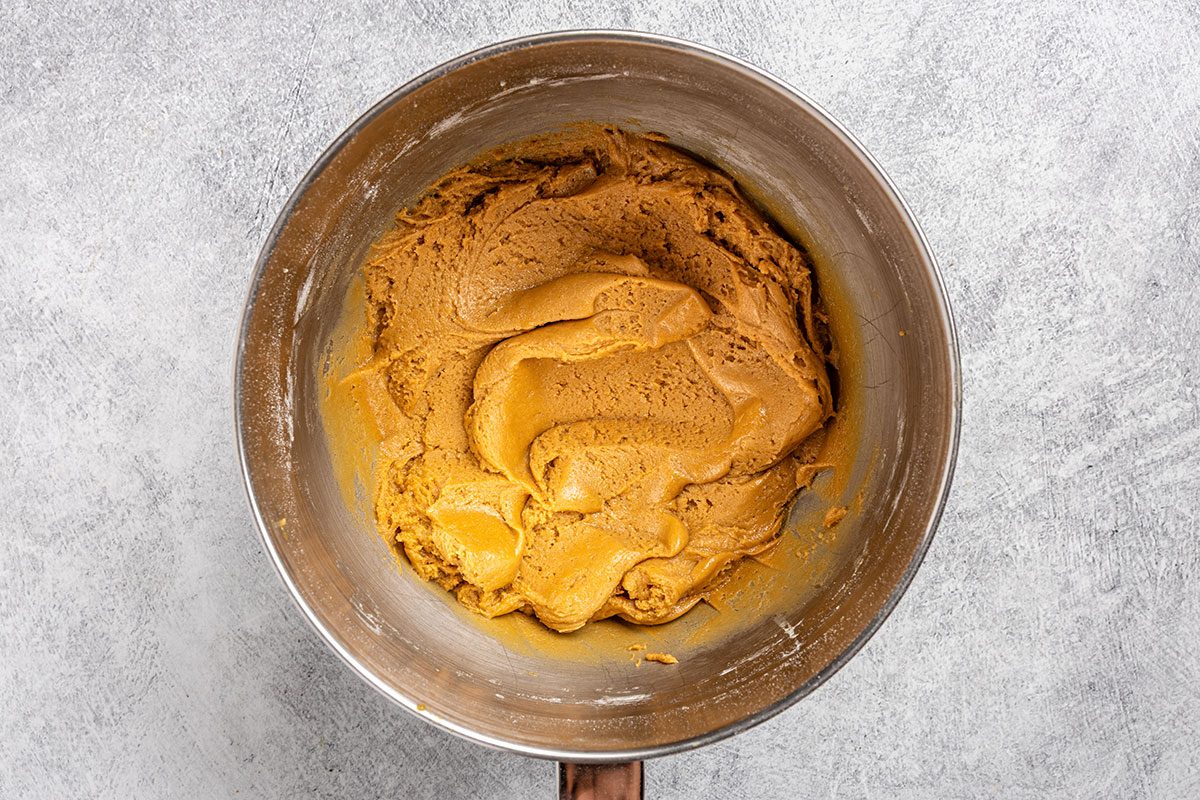 Overhead shot of a stainless steel mixing bowl filled with light brown cookie dough; resting on a light gray countertop.