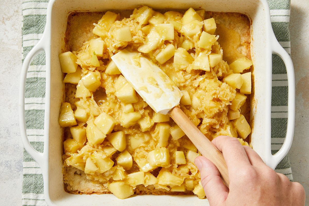 Overhead view of pear batter being spread evenly into a white square baking dish with a spatula.