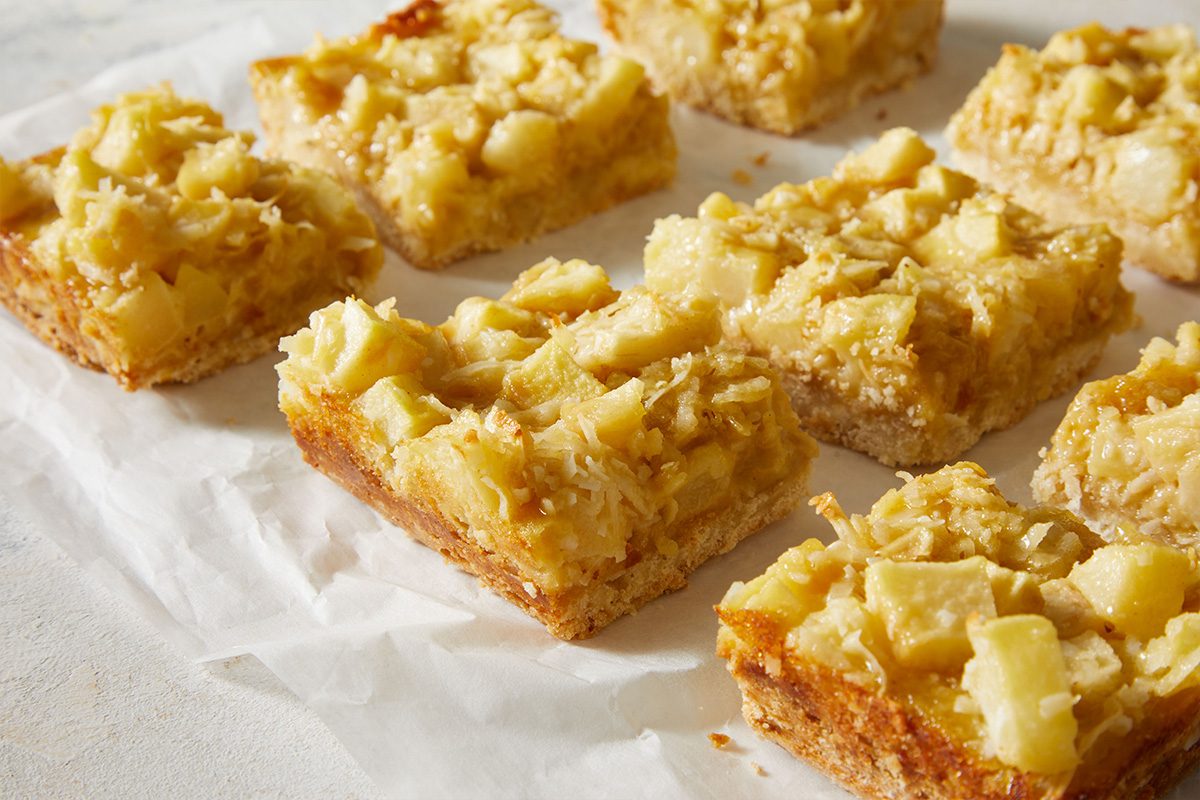 3/4 shot of golden brown Pear Bars Cookies stacked neatly on parchment paper, showing their crumbly crust and fruit topping.