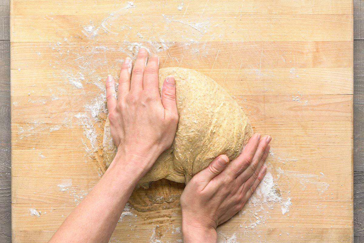 Overhead shot of two hands kneading a ball of dough on a floured wooden cutting board;