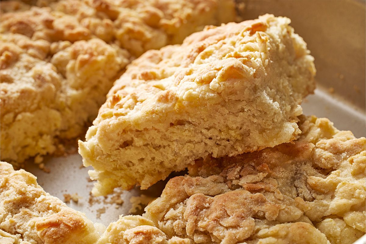 Close-up shot of a close view shows golden brown Butter Swim Biscuits one cut open and raised from the metal tray with a soft flaky layered inside visible