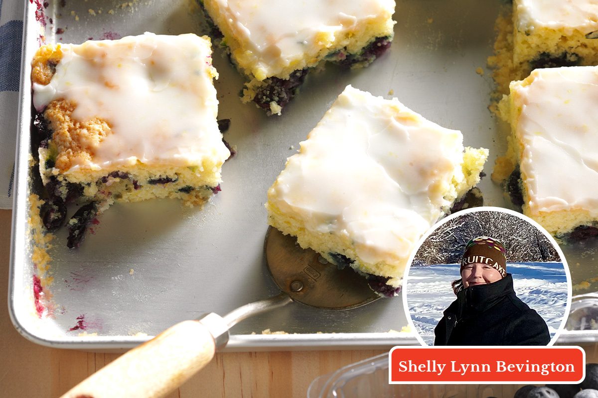 A pan of frosted square blueberry dessert bars, with one bar being lifted out. In the corner, there is a round inset photo of a person bundled up in winter clothing and the name "Shelly Lynn Bevington.