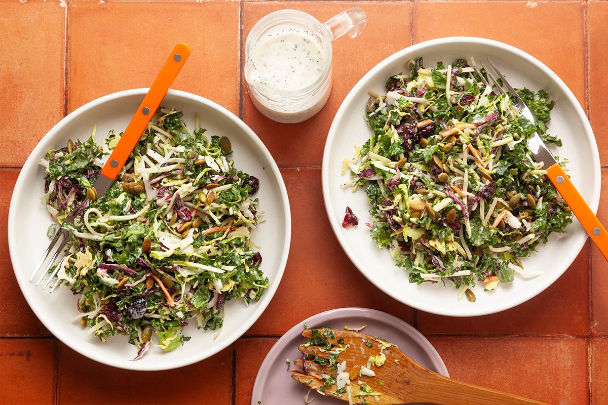 Overhead shot of Copycat Sweet Kale Salad served in two bowls, arranged on a tiled surface with dressing on the side.