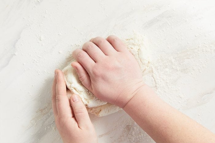 Closeup shot of hands kneading dough on a floured white surface;