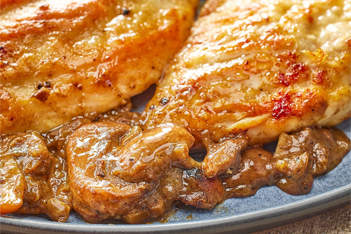 Closeup shot of a Lemon Mushroom Chicken showing two golden-brown grilled chicken breasts topped with rich chunky mushroom sauce on a gray plate;