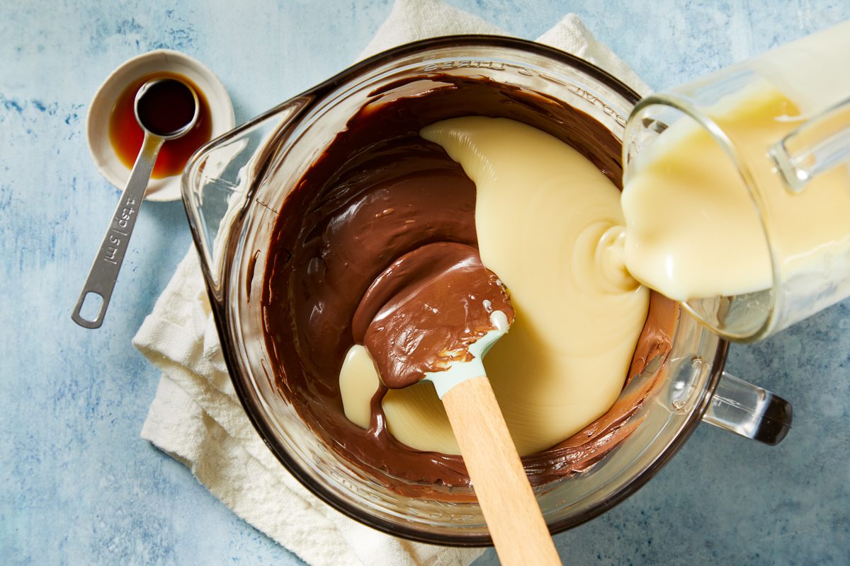 sweetened condensed milk being poured into melted chocolate mixture