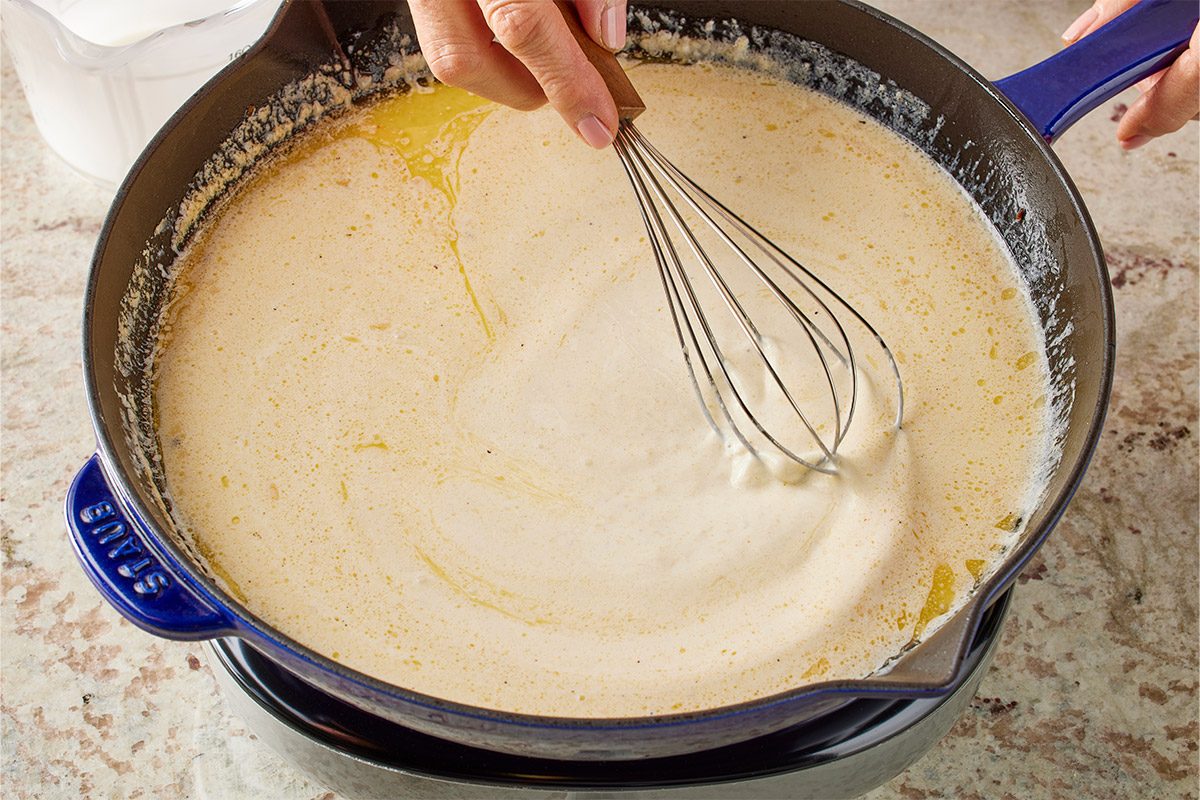 Overhead shot of a cast iron skillet holds two golden salmon fillets a hand checks one with a digital thermometer showing 165F nearby seasonings and measuring spoons lie on the counter