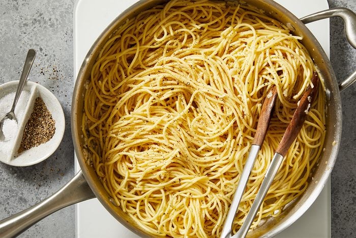 Overhead shot of spaghetti added to the skillet, being tossed to coat in the bacon-infused oil.